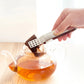 Stainless steel tea bag clip squeezing a tea bag in a glass teapot