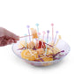 Hand placing pastel cartoon cake forks into fruit bowl