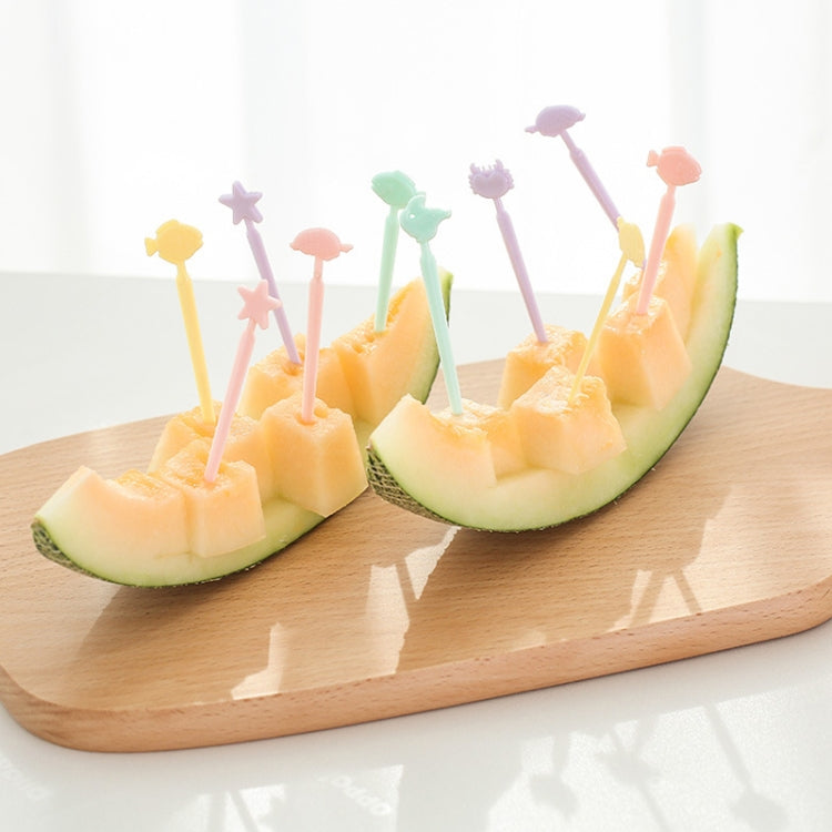 Pastel cartoon cake forks inserted into fruit melon halves on wooden tray