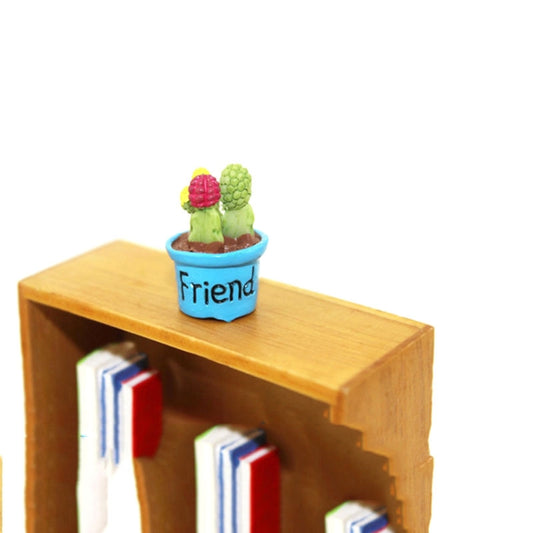 Mini potted artificial cactus in blue pot labeled Friend on a wooden shelf