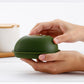 Avocado-green plastic crisper container held by hands with lid closed.