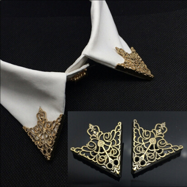 Ornate triangular collar buckle pair on a white shirt cuff, gold-tone filigree