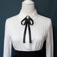 White shirt collar with black ribbon bow tie and round faux-pearl brooch