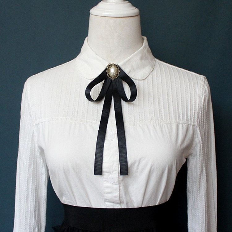 White shirt collar with black ribbon bow tie and round faux-pearl brooch