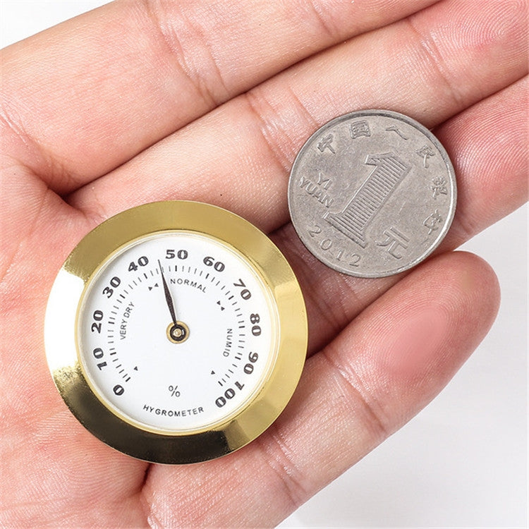 Gold 38mm hygrometer gauge held in hand, shown with coin for size