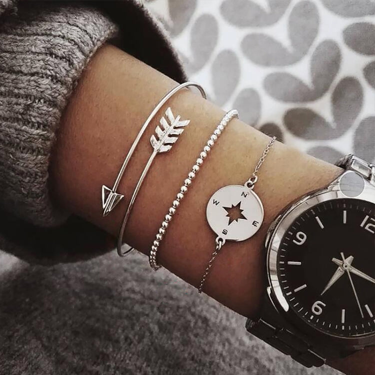 Silver-toned bracelets stacked together with arrow and compass circle charms on wrist