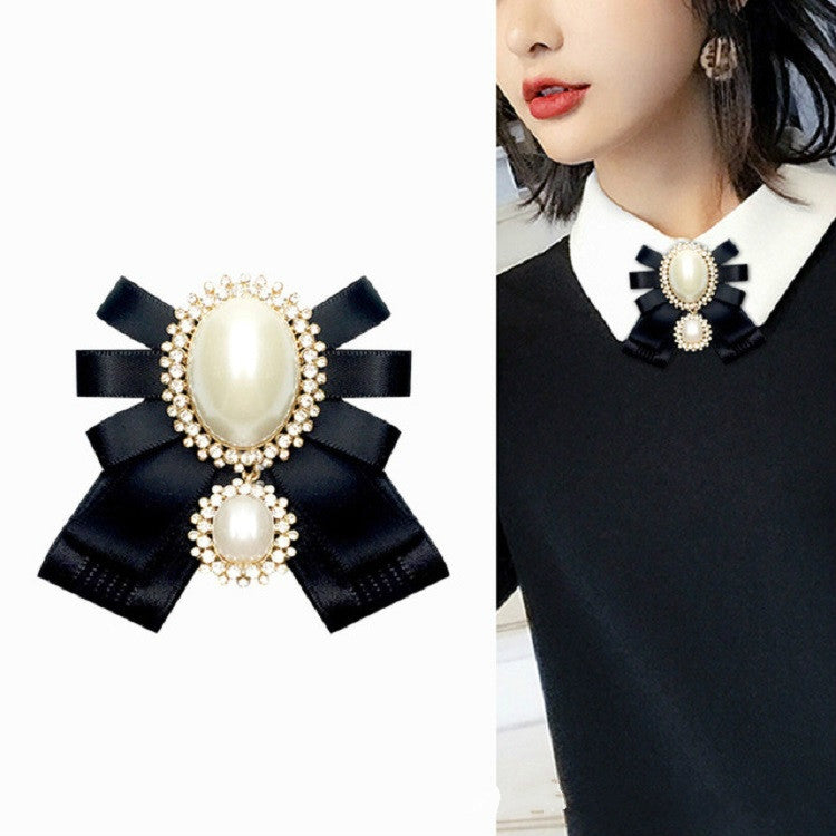 Bow brooch worn on a white-collared top: black ribbon with oval pearl and rhinestones