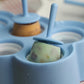Blue silicone ice mold tray holding a green ice cube with a stick.