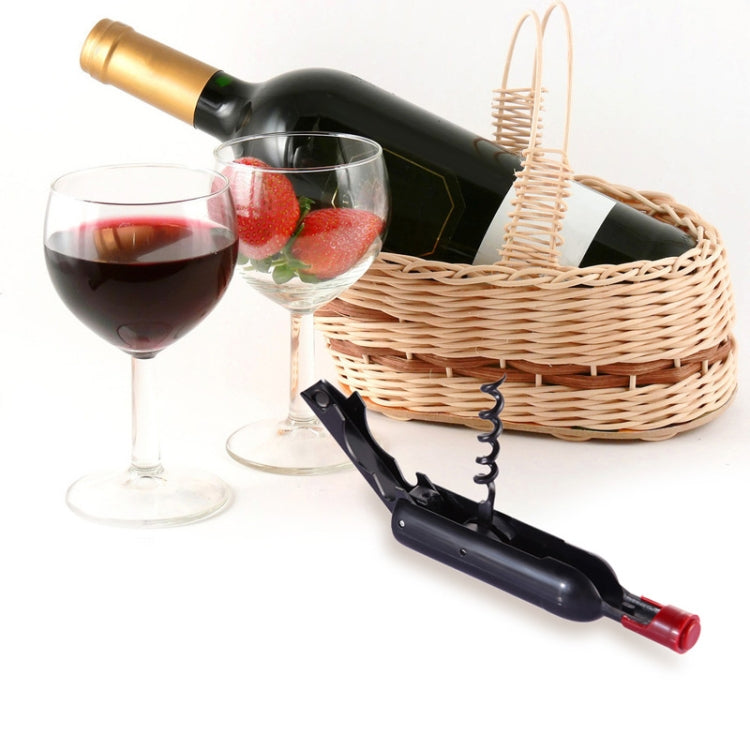 Black and red bottle opener with corkscrew on a tabletop beside wine bottles