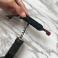 Black bottle opener held by hand, corkscrew inserted into a bottle cork