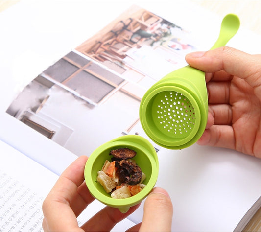 Green dinosaur tea infuser strainer, held open with perforated basket on paper.