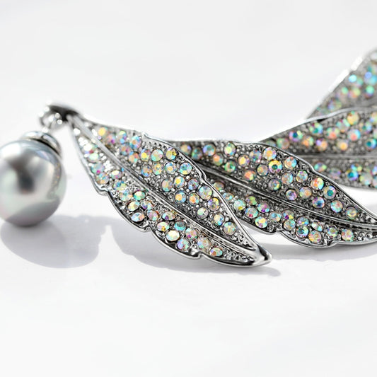 Close-up of silver feather brooch with multicolor rhinestone details and pearl