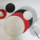 Set of round woven placemats in black, red, white, and gray