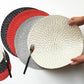 Round woven placemat stack in beige, gray, and black with red accents