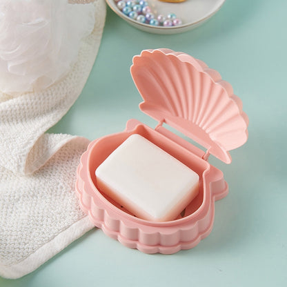 Pink seashell soap dish with flip lid and drain slots, holding a bar of soap