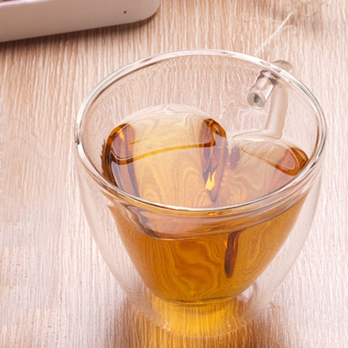 Heart-shaped double-wall glass mug with amber tea, clear lidless cup and handle