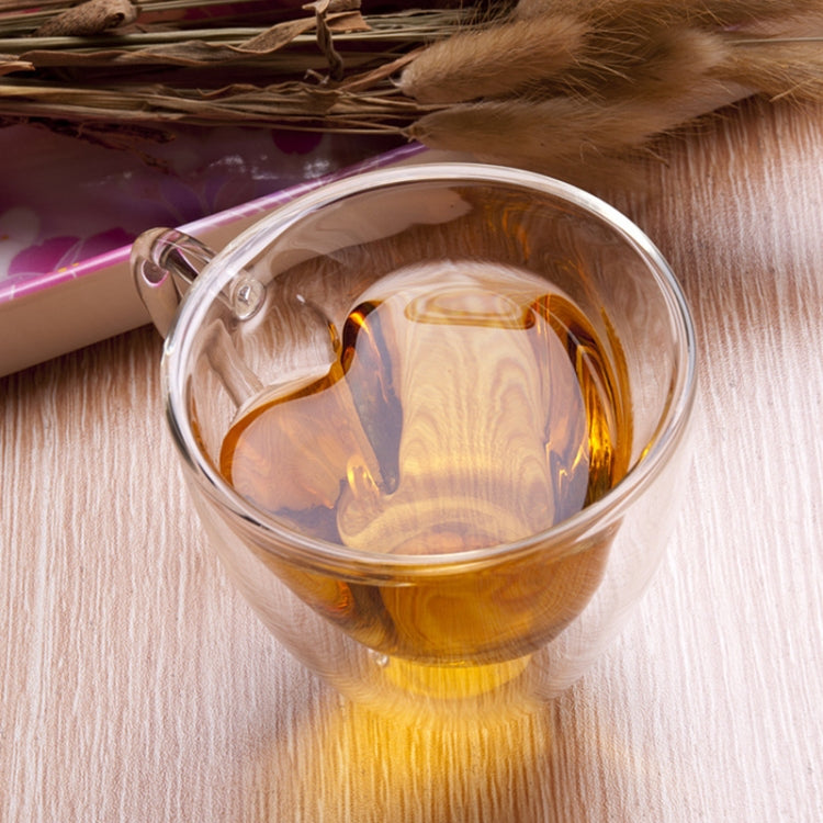 Heart-shaped double-wall glass mug holding amber tea with visible heart silhouette