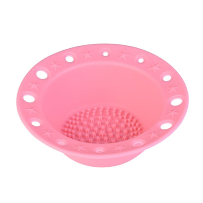 Pink silicone makeup brush cleaning bowl with textured scrubbing pad and draining holes.