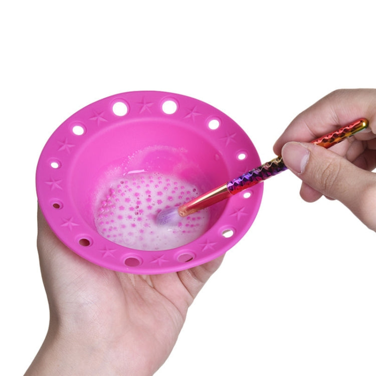 Pink silicone makeup brush cleaning bowl with textured scrubbing pad and hand-held brush.