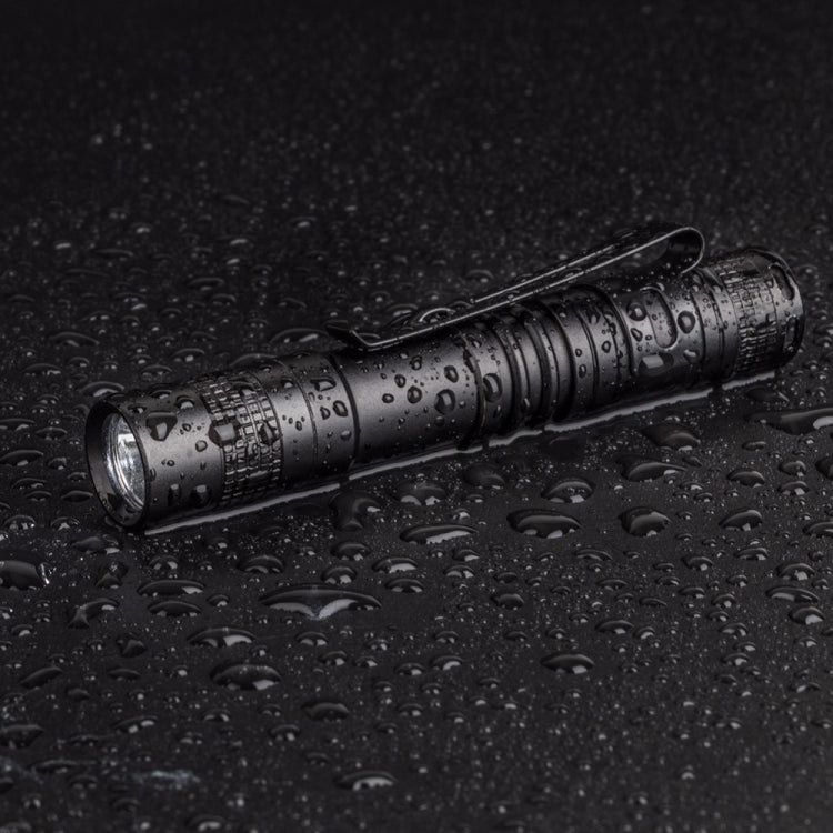 Black pen-shaped LED flashlight on wet surface with water droplets
