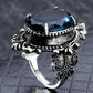 Silver-tone ring side view with blue faceted stone in ornate raised band