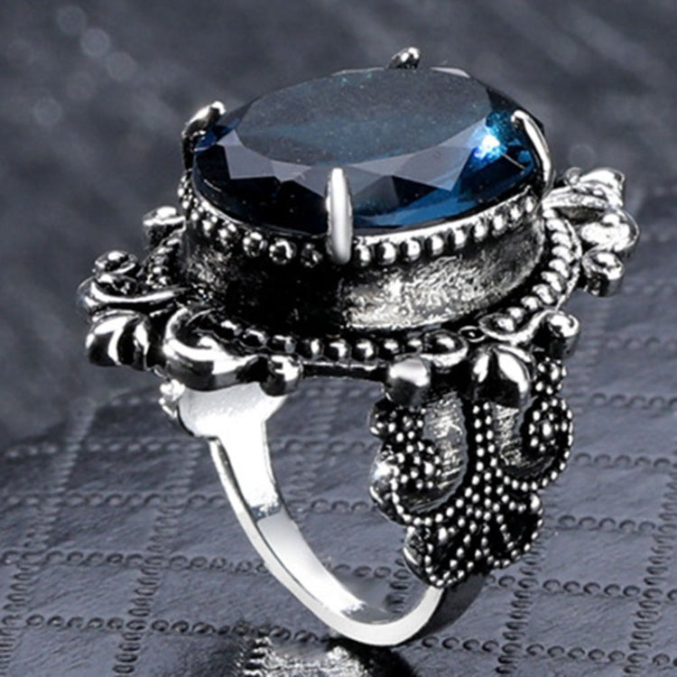 Silver-tone ring side view with blue faceted stone in ornate raised band