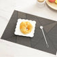 Dark gray check table mat with textured weave, featuring a white plate and small spoon.