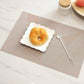Beige geometric check table mat with textured weave, featuring a white plate and spoon.