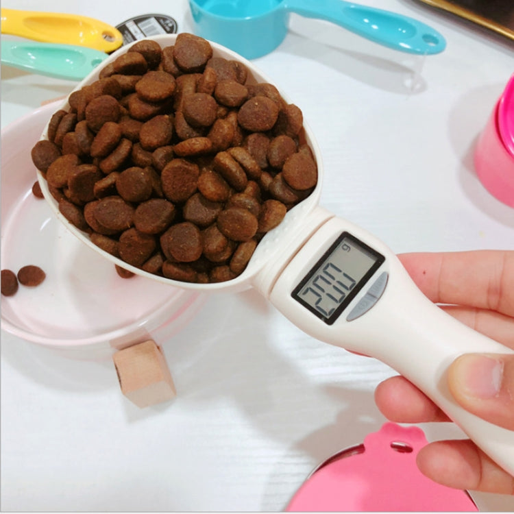 Electronic pet food measuring spoon weighing dry kibble, LCD screen visible