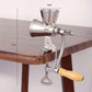 Stainless steel manual grinder mounted on a tabletop with wooden handle