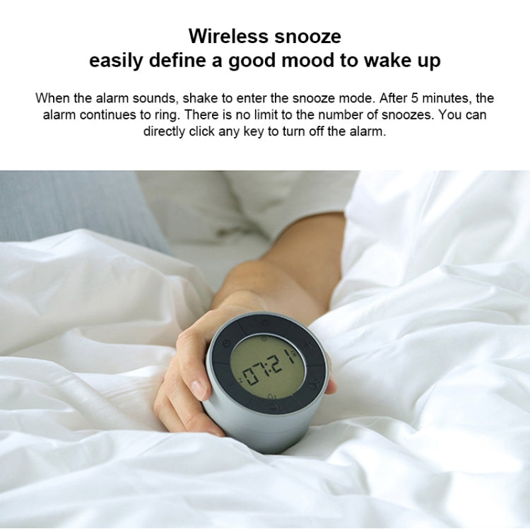Light gray alarm clock night light with round LCD time display on a bed.