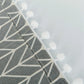 Corner close-up of dark gray microwave cover with white arrow pattern and pom trim