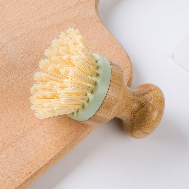 Dish scrubber brush with cream bristles and green band on wooden handle, angled view