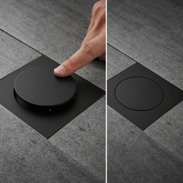 Foot-operated floor drain with black square base and round lid, hand pressing