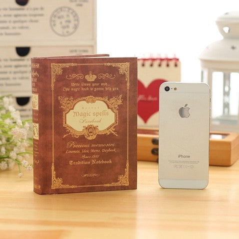 Brown vintage pocket notebook with gold spell text cover, standing on desk.
