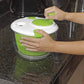 Salad spinner on countertop with hands pressing the green top lid and knob