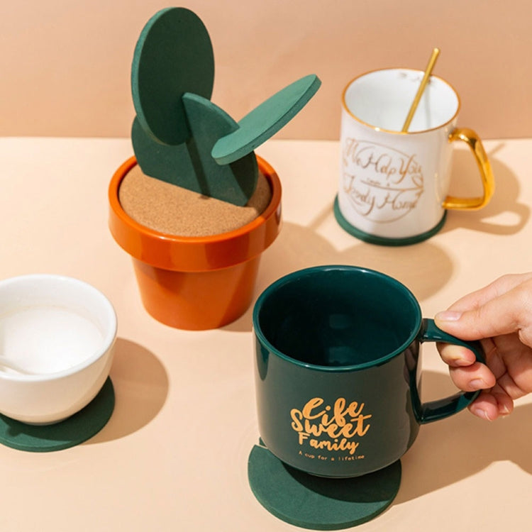 Cactus coaster next to cups: green felt cactus on cork base in an orange pot.