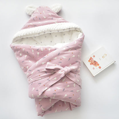Baby holding blanket with pink cartoon print, white fleece trim, and tied bow hood