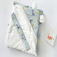 Baby holding blanket with light blue cartoon print, white fleece trim, and side strap