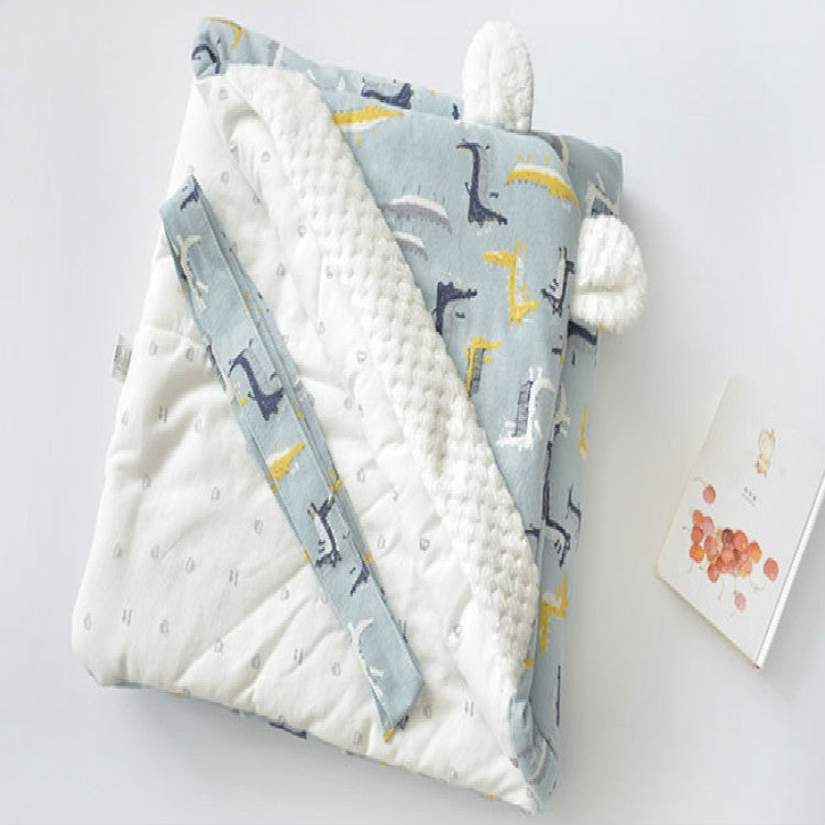 Baby holding blanket with light blue cartoon print, white fleece trim, and side strap