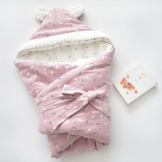 Baby holding blanket with pink cartoon print, white fleece trim, and tied bow hood