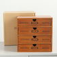 Wooden drawer storage cabinet with four drawers and arched pulls; cardboard box behind.