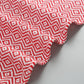 Corner view of red-and-white zigzag cotton bath towel with tassel edge