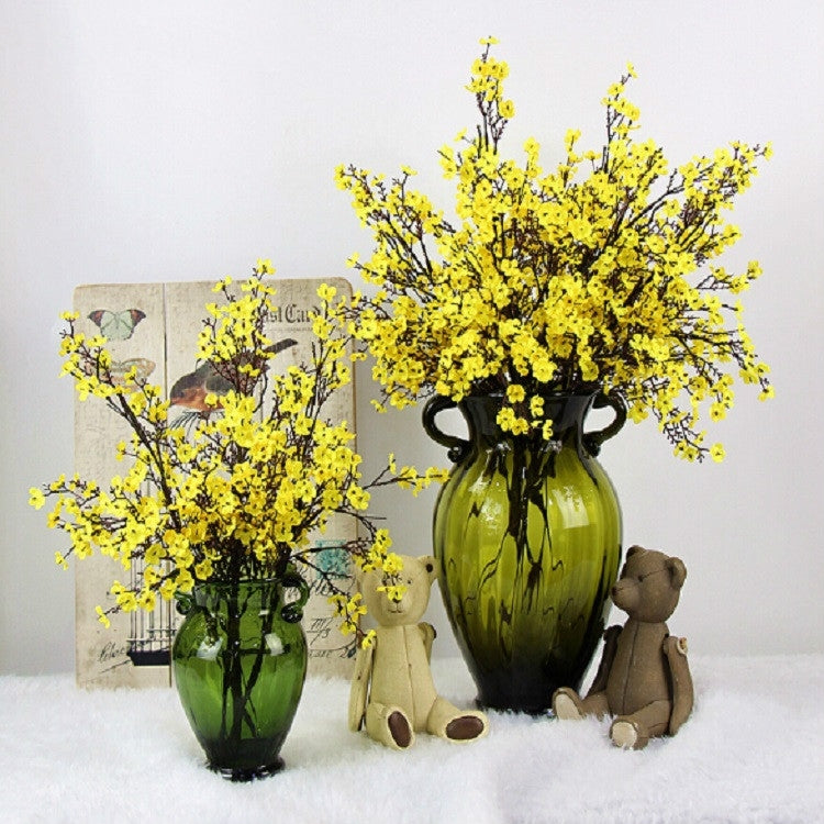 Yellow artificial blossom branches in dark green glass vase with teddy bear figurines