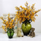 Orange artificial blossom branches in dark green glass vase with teddy bear figurines