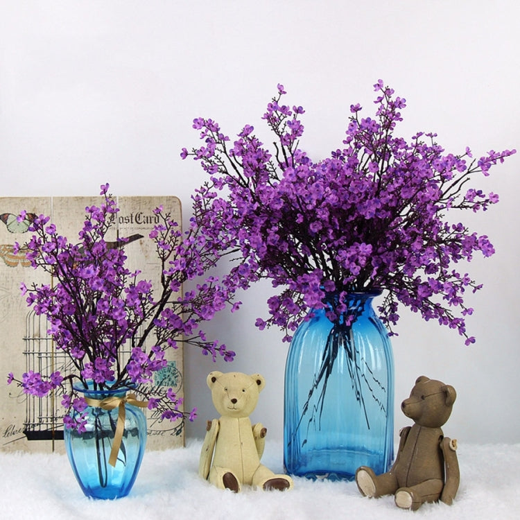 Purple artificial blossom branches in light blue glass vase with teddy bear figurines