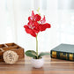 Red faux Phalaenopsis orchid in a white round pot with green leaves