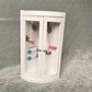 White dollhouse bathroom cabinet with two doors, blue towel bars, and gold fixtures