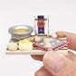 Mini chopping board held by hand, with toy bread, eggs, and metal blister tray