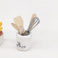 Mini kitchen utensil set close-up: white crock with metal whisk and wooden spatulas